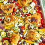 bone in, skin on chicken thighs nestled on a sheet pan with tomatoes and peppers, kalamata olives, and feta cheese.