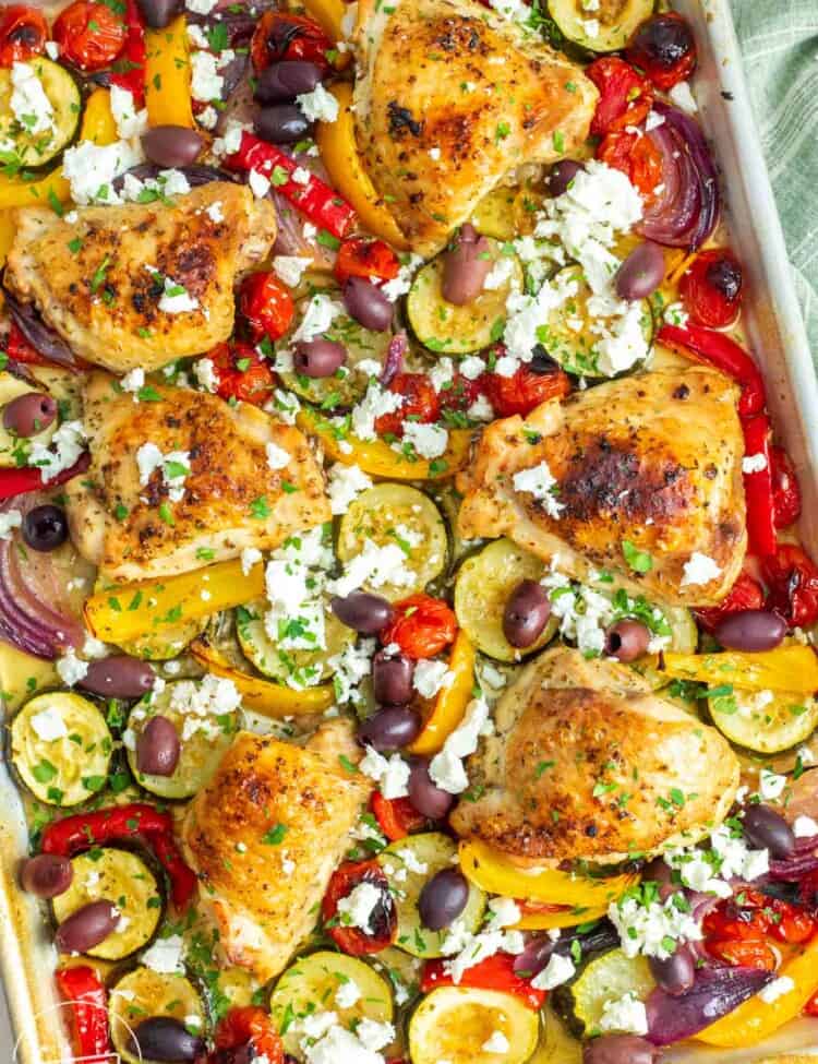bone in, skin on chicken thighs nestled on a sheet pan with tomatoes and peppers, kalamata olives, and feta cheese.