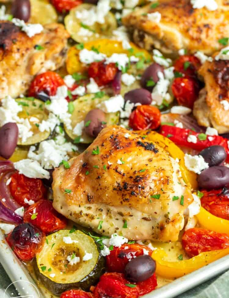 closeup of greek chicken with vegetables cooked together on a sheet pan.