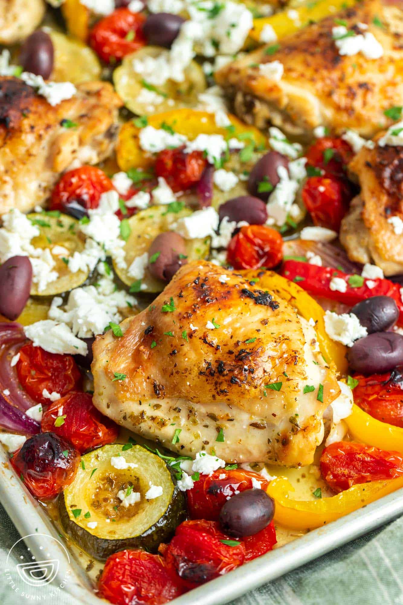 closeup of greek chicken with vegetables cooked together on a sheet pan. 