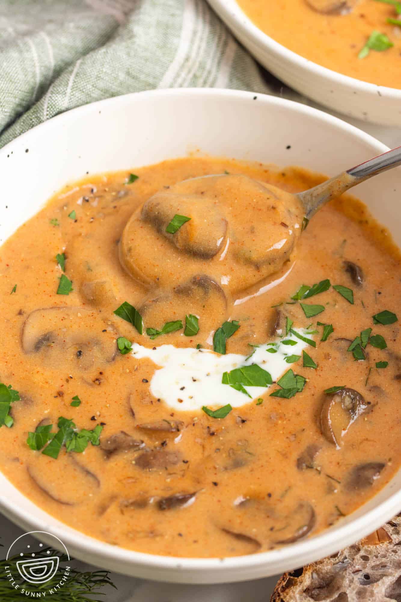 a white bowl of brown creamy soup with mushrooms. A spoon is taking a bite. 