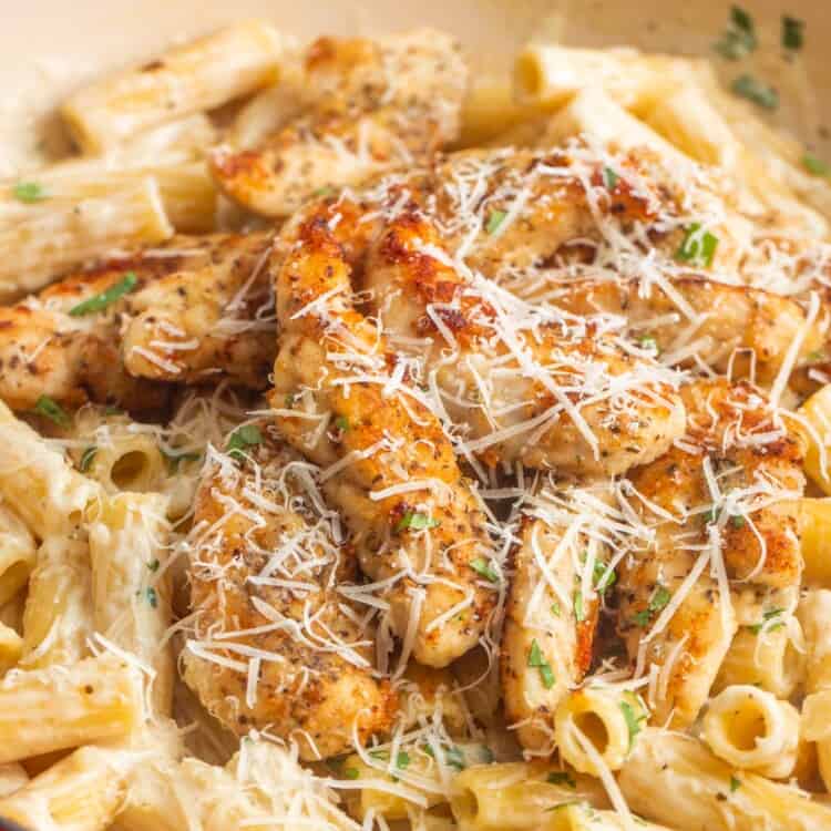 a red enameled skillet of parmesan chicken tenderloins over creamy ziti pasta. The dish is topped with fresh parsley and grated cheese.