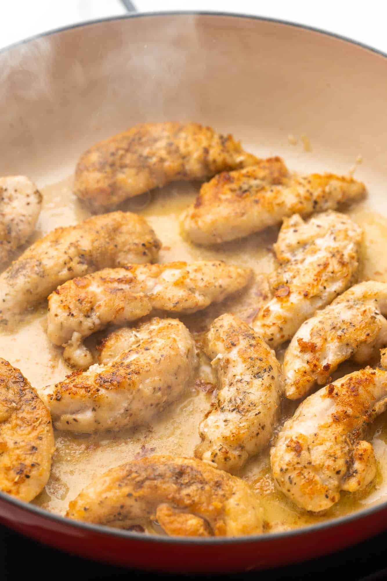chicken tenders cooking in a red and white skillet until browned.