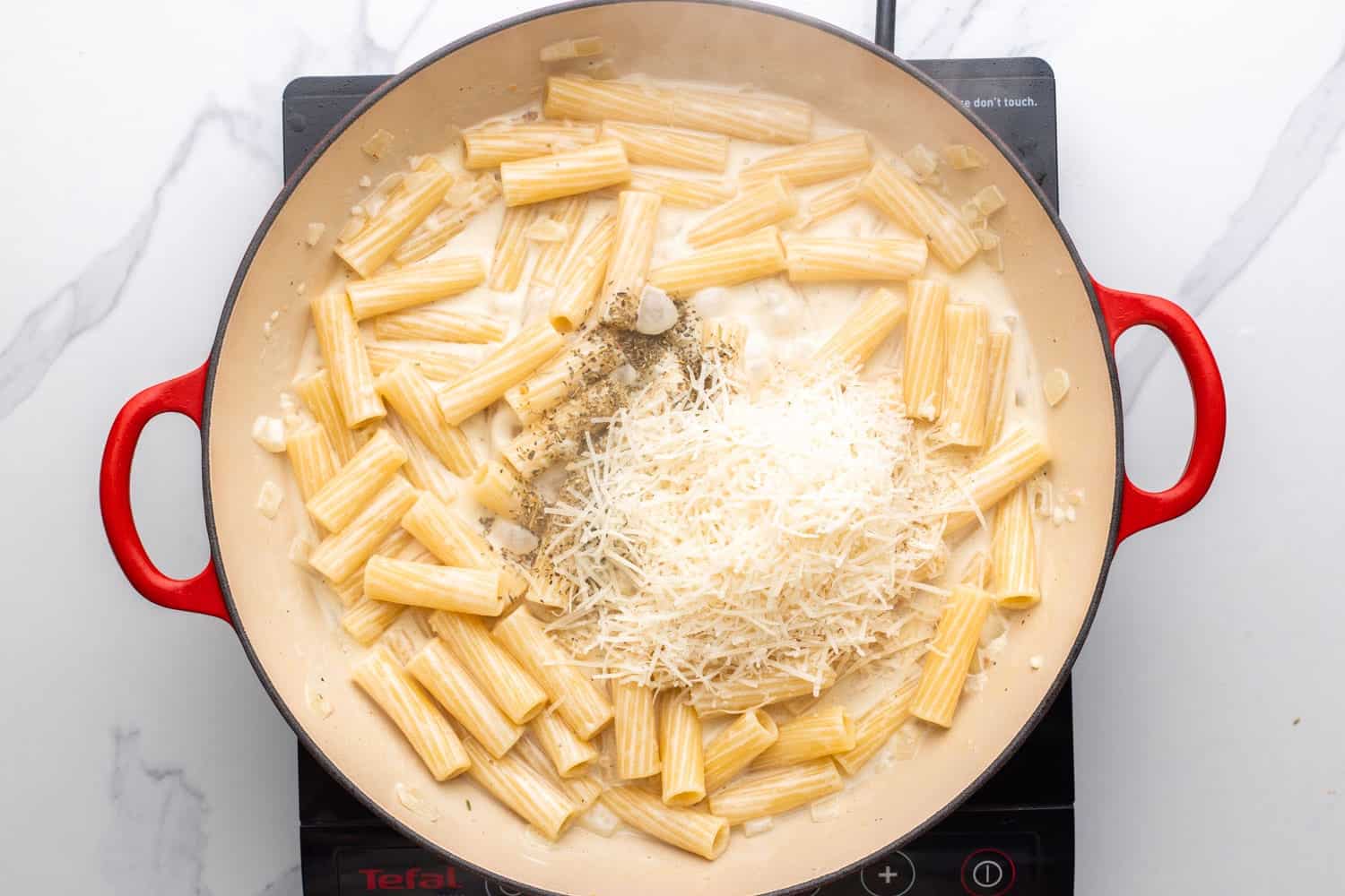 parmesan cheese, salt, and pepper added to creamy parmesan pasta in a skillet, viewed from overhead.