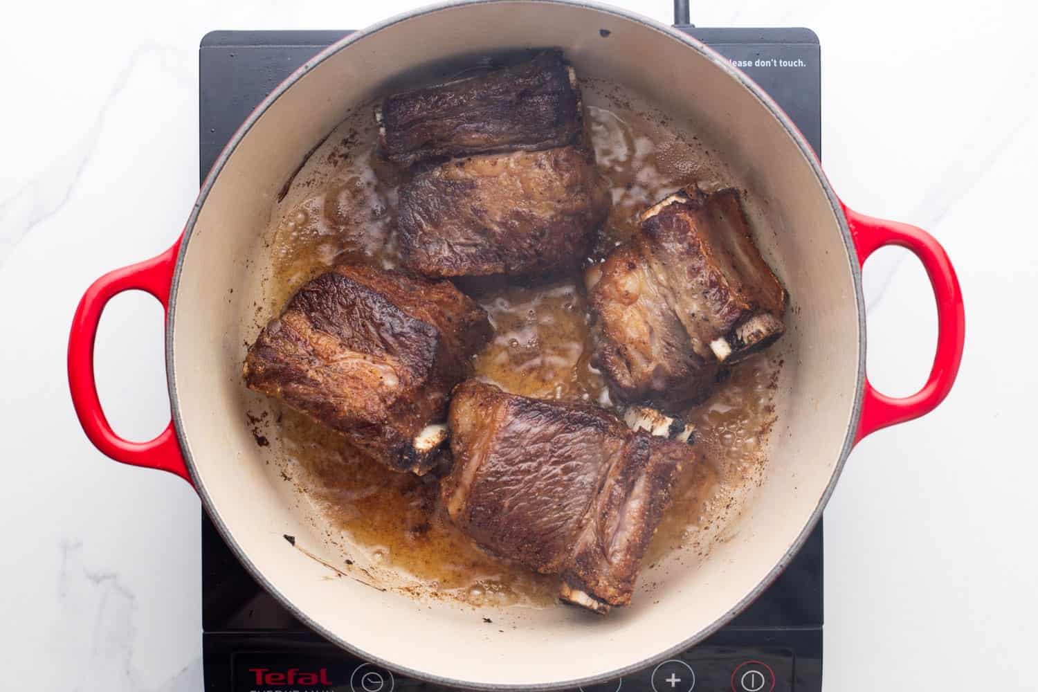 a dutch oven holding oil and seared beef short ribs.