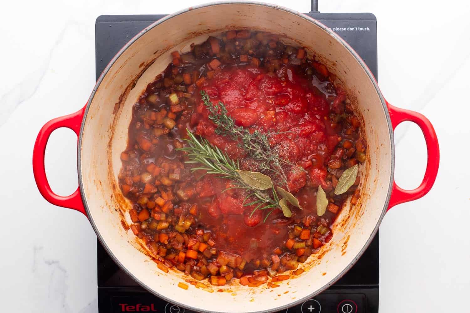 tomatoes and fresh herbs added to a pot of ragu. 