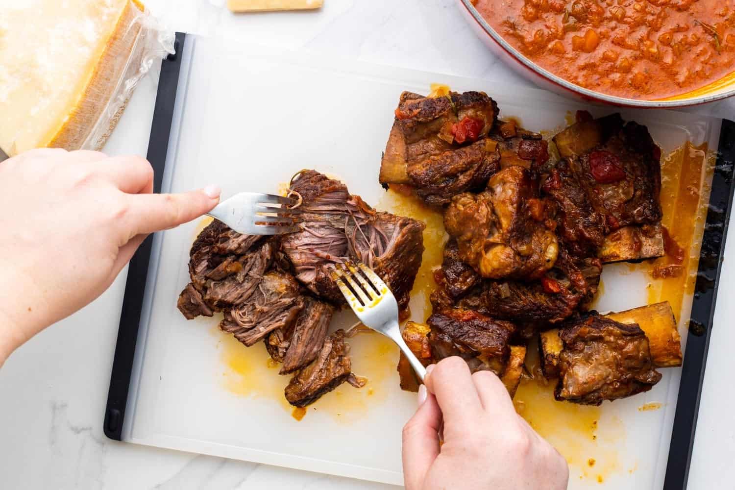 a person shredding beef short ribs with two forks on a cutting board. 
