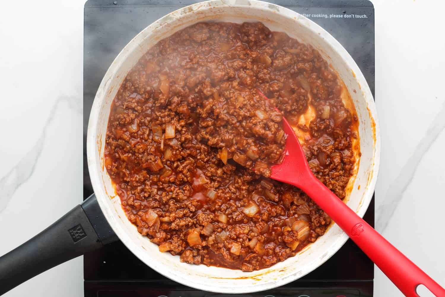 homemade sloppy joe mixture in a skillet, stirred with a red spatula spoon. 