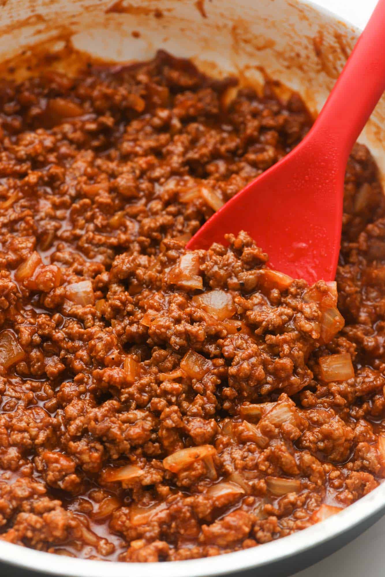 a closeup of homemade sloppy joes in a skillet, stirred with a red spoon. 