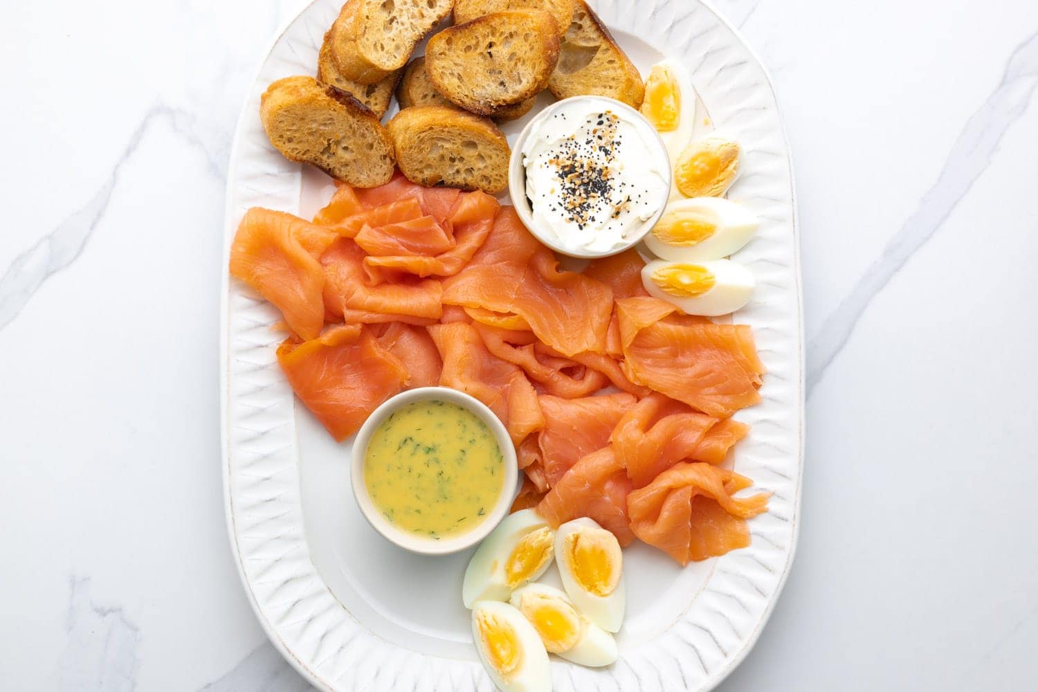 Quartered hard boiled eggs, crispy bread, sliced smoked salmon, and two types of sauces on a platter.