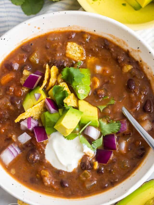 overhead view of a bould of black bean soup topped with sour cream, avocado, onion, and cilantro.