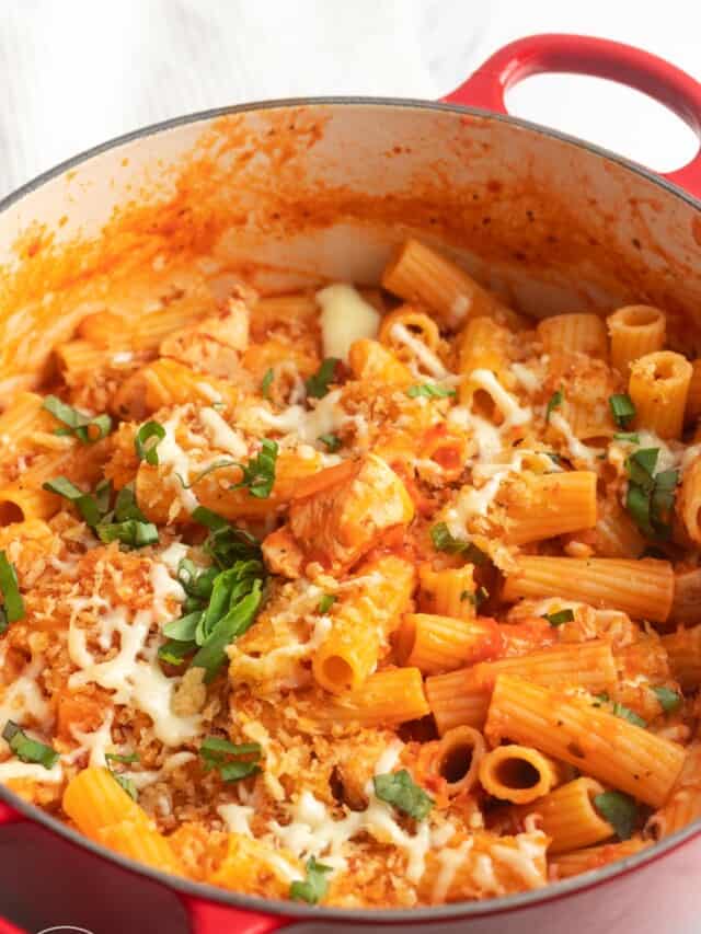 a large dutch oven filled with rigatoni and chicken in a tomato sauce, topped with cheese and breadcrumbs