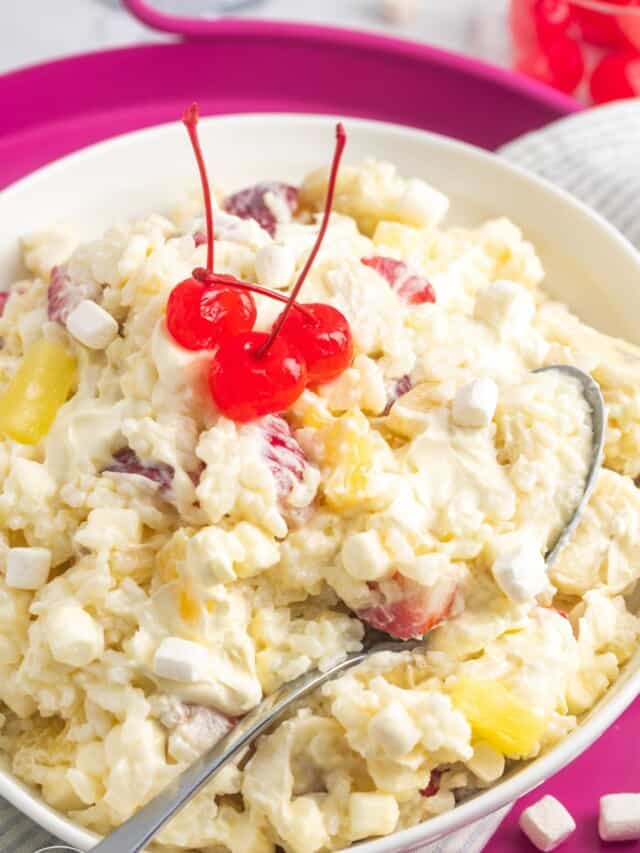 a white serving bowl of rice with fruit and whipped cream, on a pink charging plate.