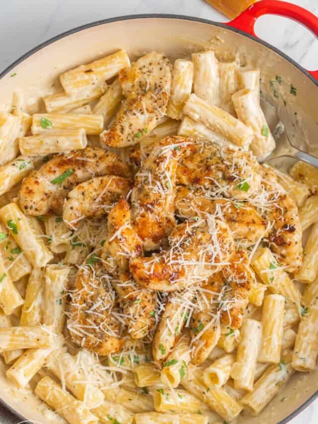 a large enameled cast iron skillet holding creamy ziti pasta and pan seared chicken tenderloins, topped with parmesan cheese.