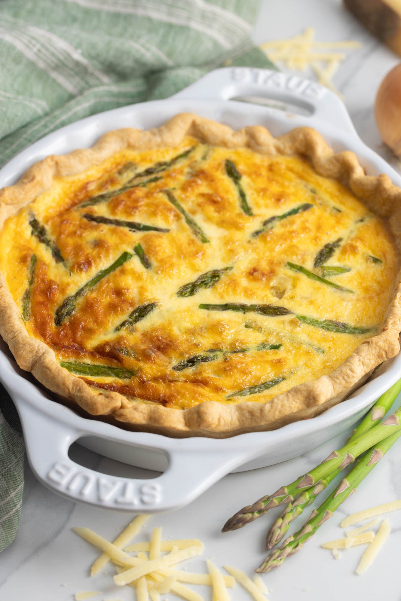a baked asparagus quiche in a white ceramic pie plate. It's golden brown on top.