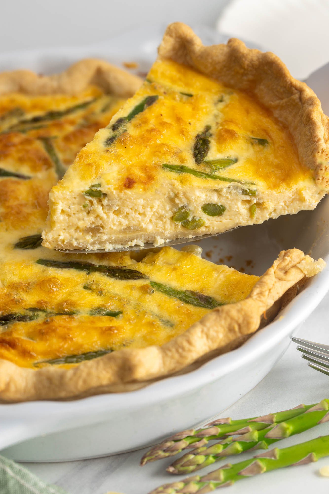 a slice of asparagus quiche lifted from the pan with a cake server.