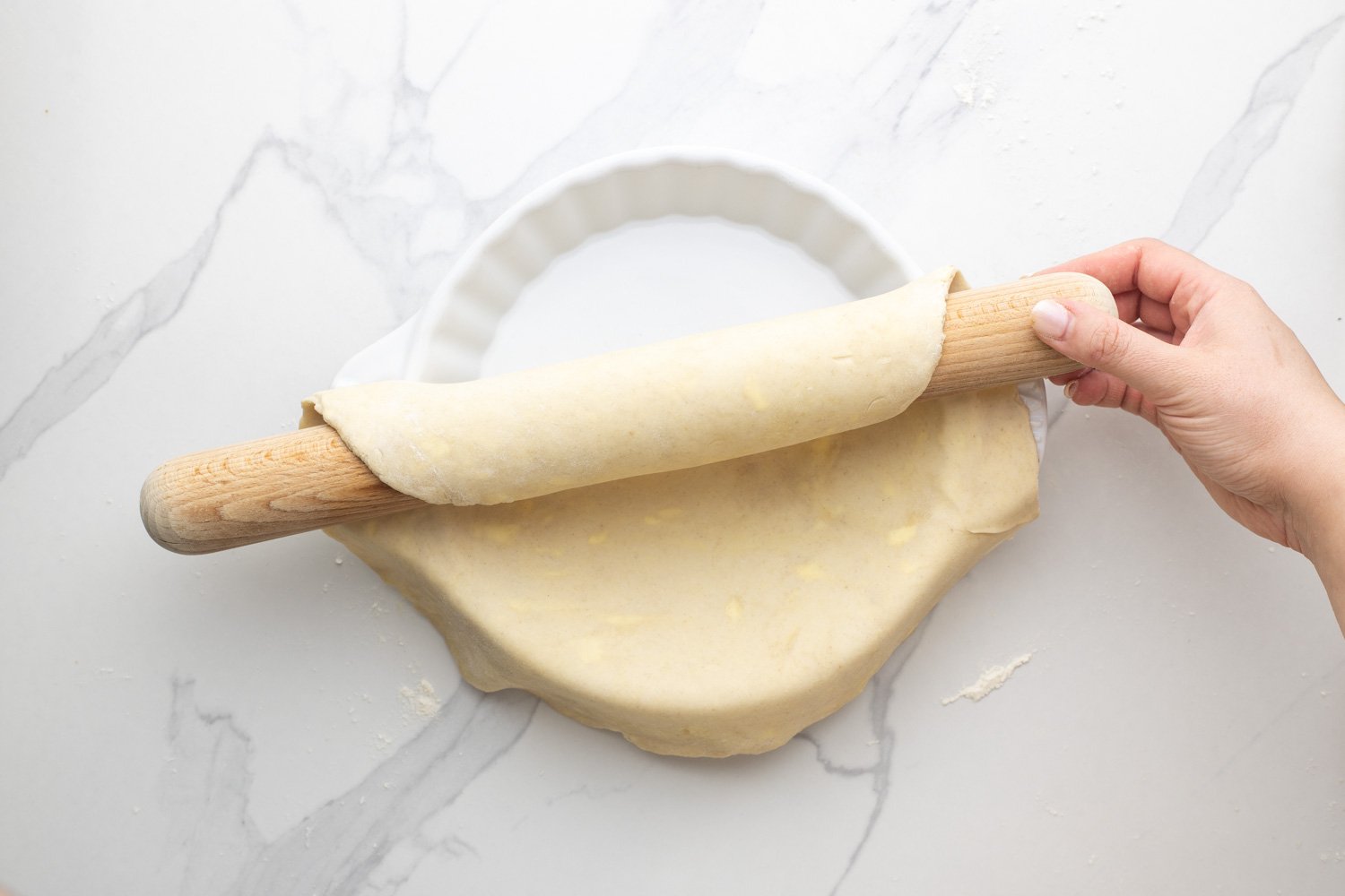 crust dough added to a fluted pie pan with a wooden rolling pin for support.