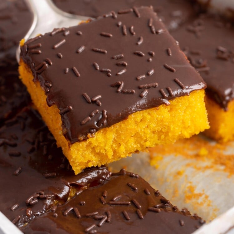 a square piece of carrot cake with chocolate frosting lifted out of the pan.