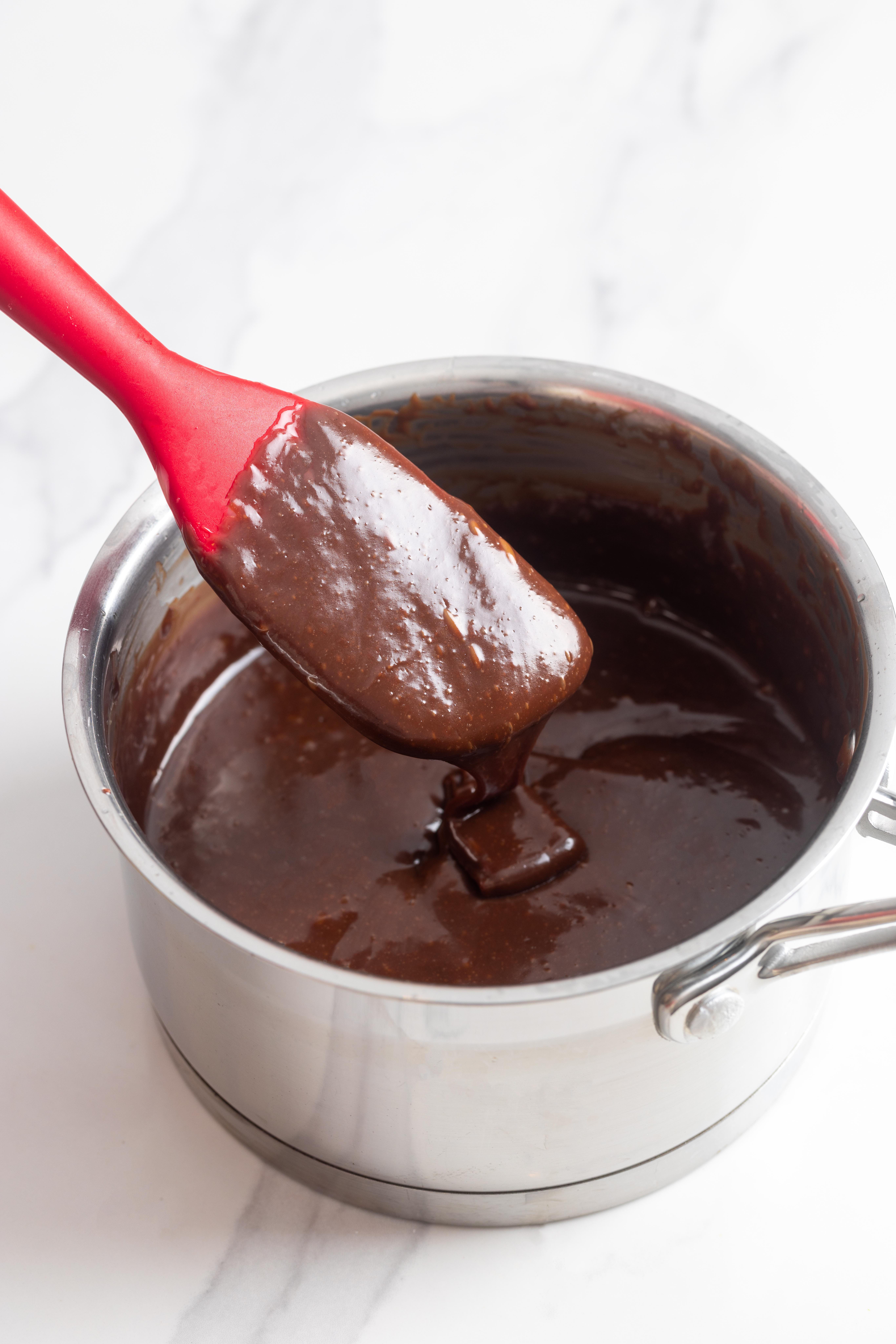 Chocolate glaze for carrot cake in a small pot with a spatula.