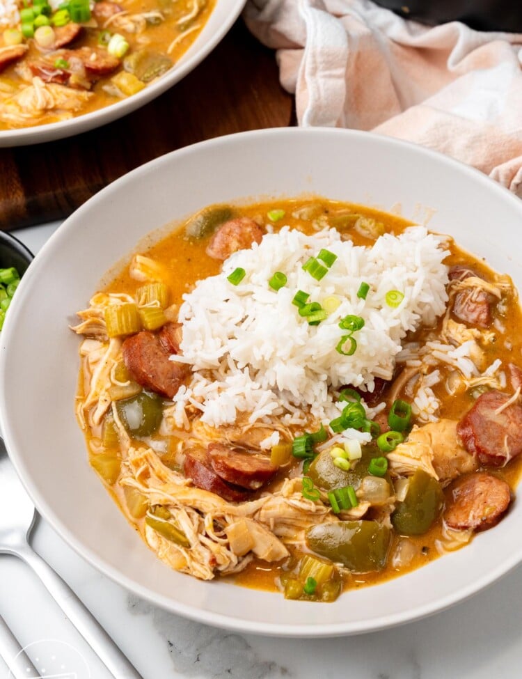 a plate of sausage and chicken gumbo with rice on a marble counter.