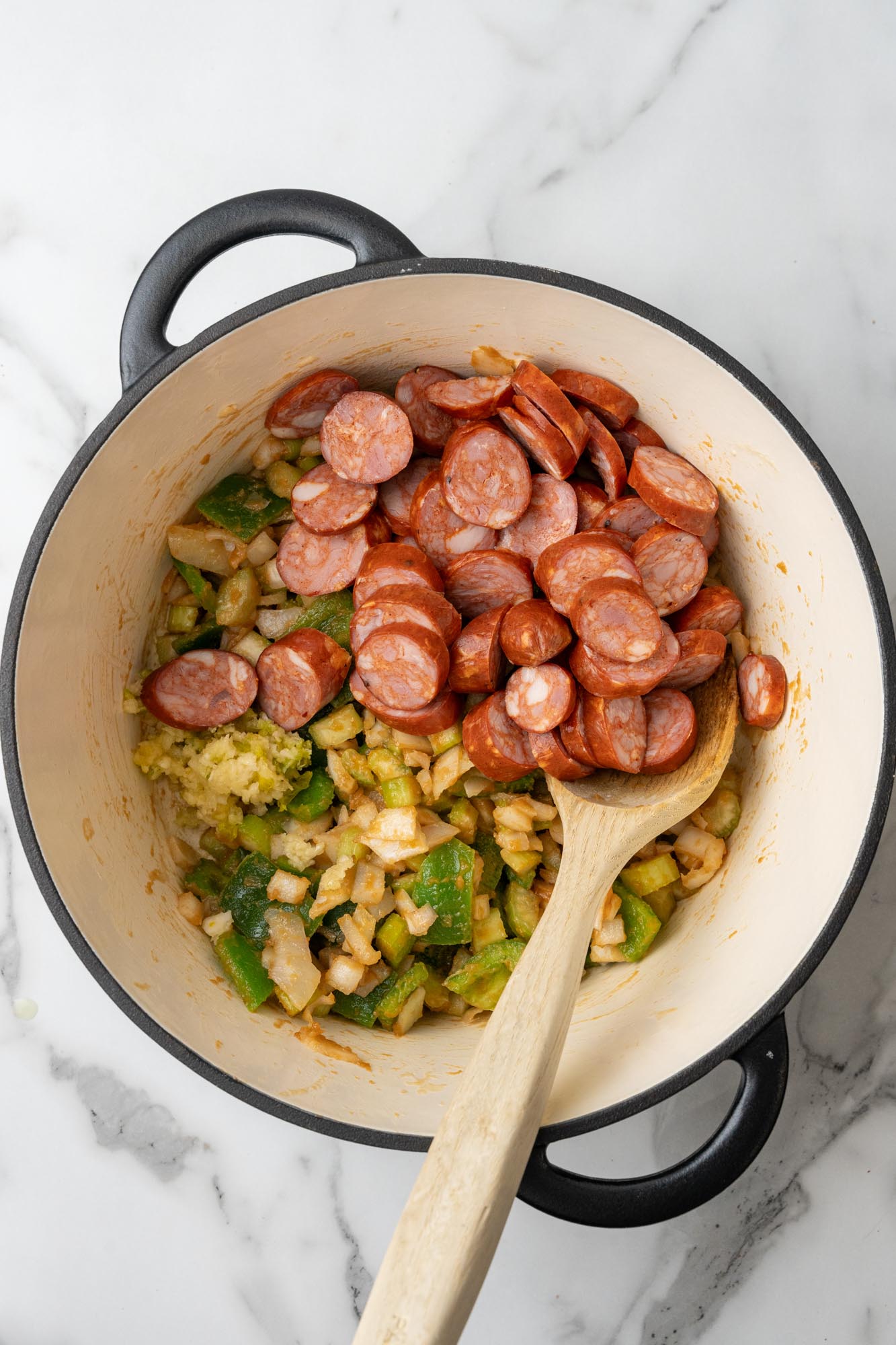 sliced andouille sausage added to a pan of onions and peppers cooked in roux.