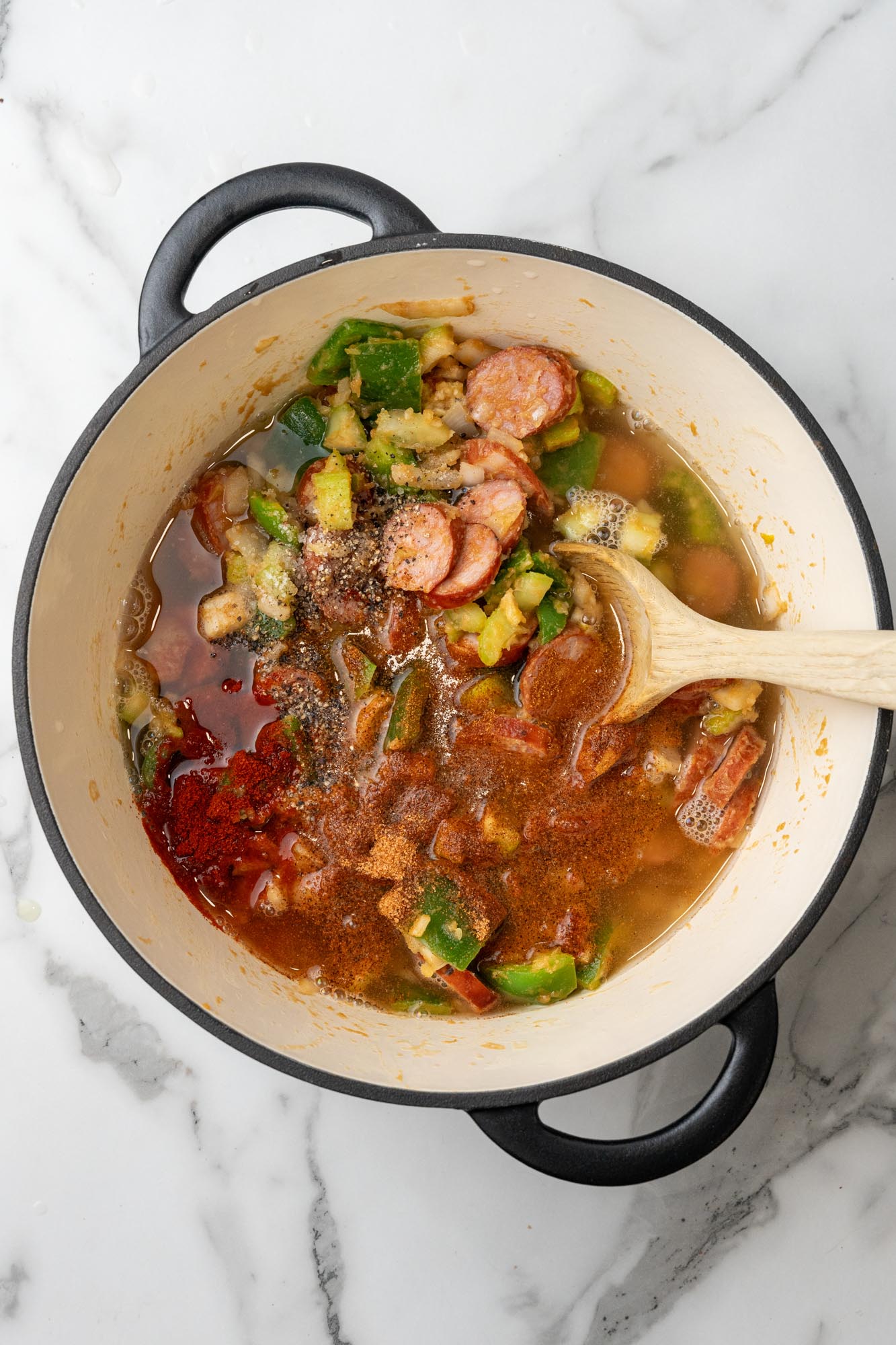 broth and seasonings added to a dutch oven filled with veggies and sausage.