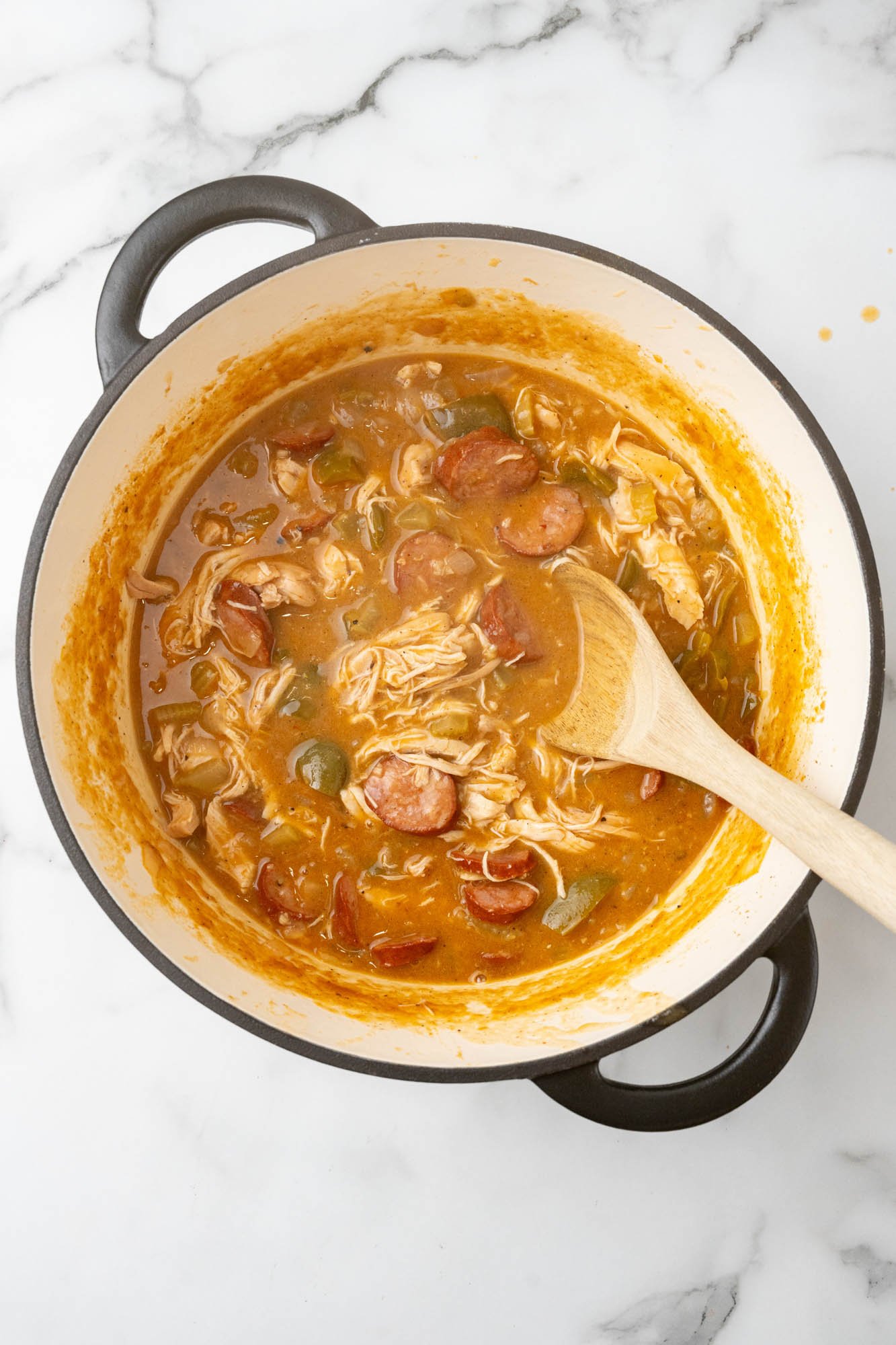 chicken and sausage gumbo simmering in a dutch oven, stirred with a wooden spoon