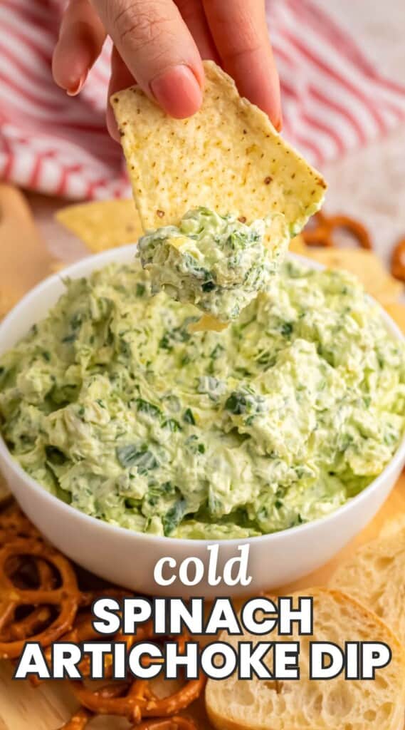 a bowl of creamy spinach artichoke dip. A hand is dipping a chip into the dip. Text overlay at bottom of image says "cold spinach artichoke dip"
