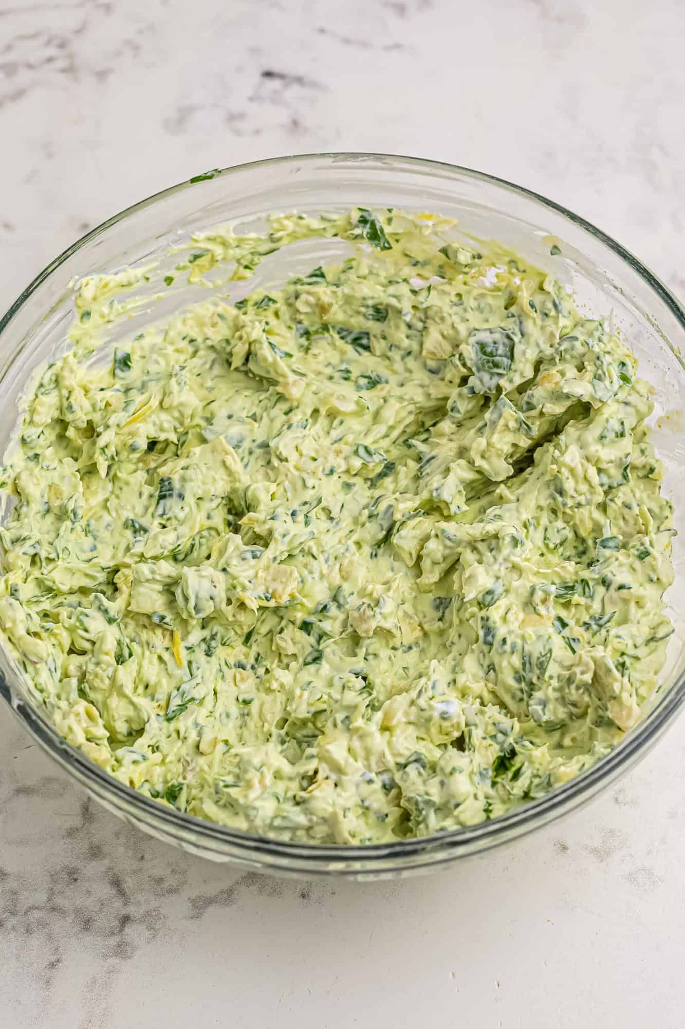 cold spinach artichoke dip in a glass mixing bowl.