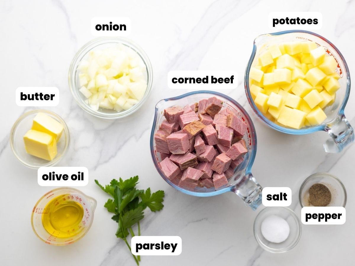 The ingredients for corned beef hash all measured into small bowls and arranged on a counter. Corned beef, onions, and potatoes are diced into small cubes.