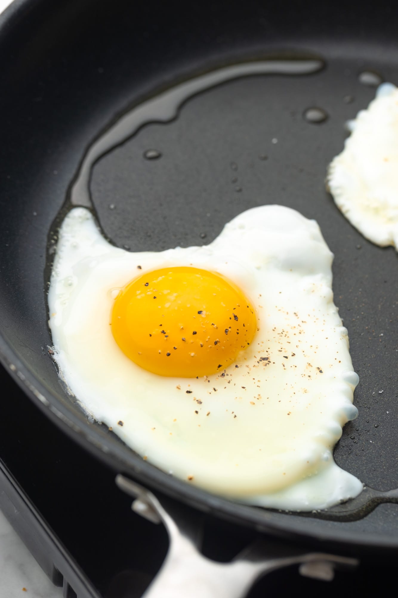 a fried egg cooking in a nonstick pan with oil.