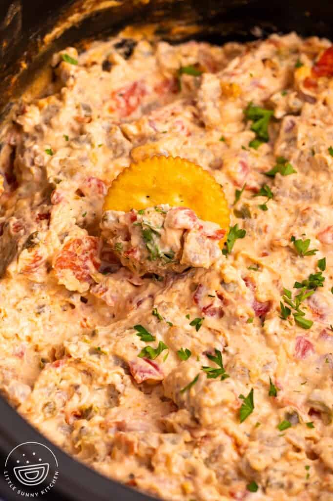 creamy pizza dip in a black crockpot. There is a cracker in the dip.