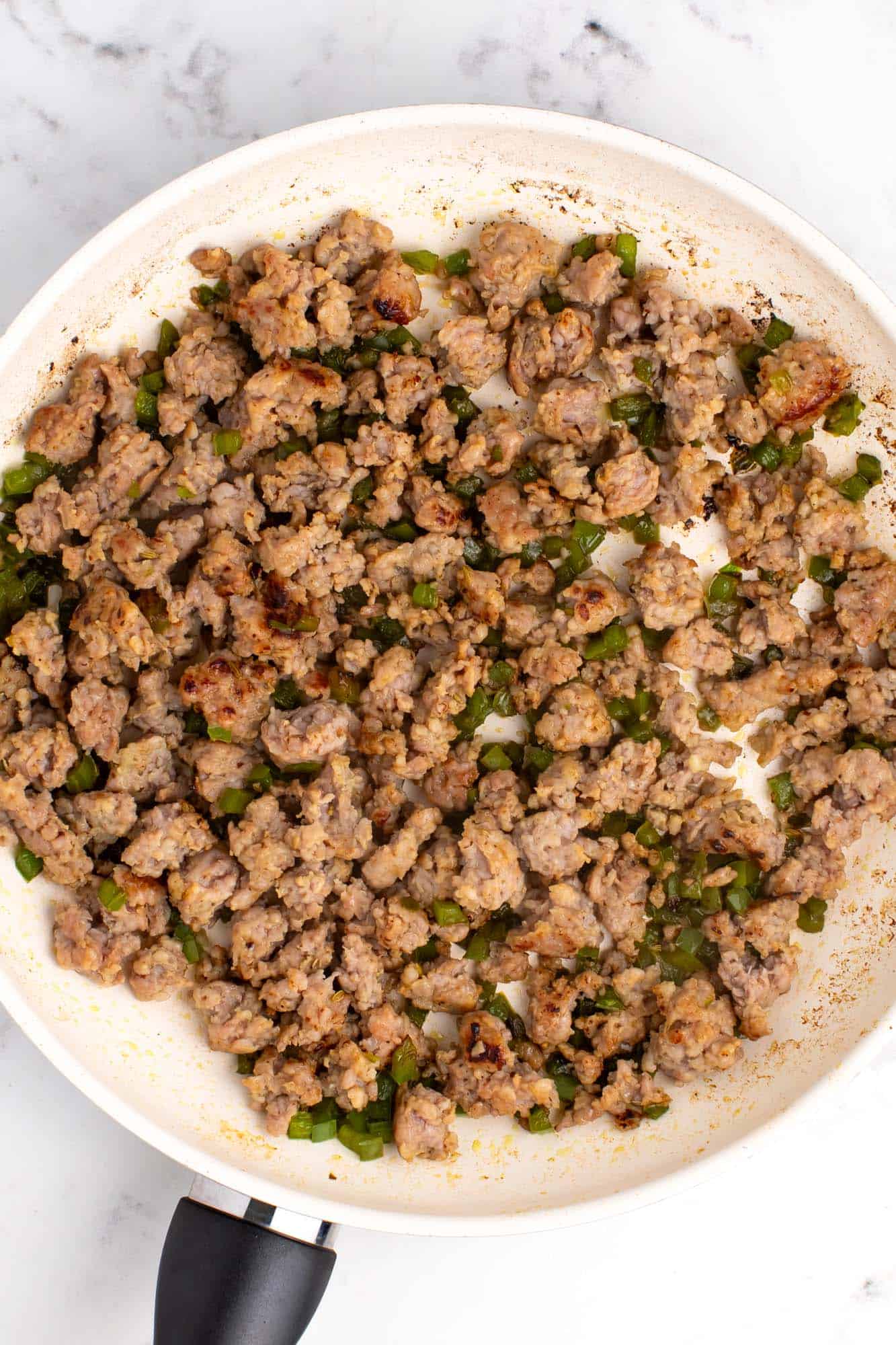 crumbled italian sausage cooked with peppers in a white enameled skillet