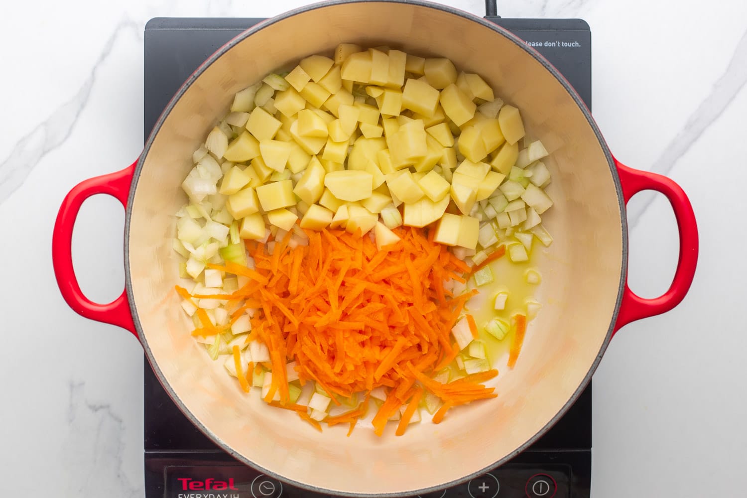 a dutch oven on an electric burner holding oil, shredded carrot, diced potato, diced onions.