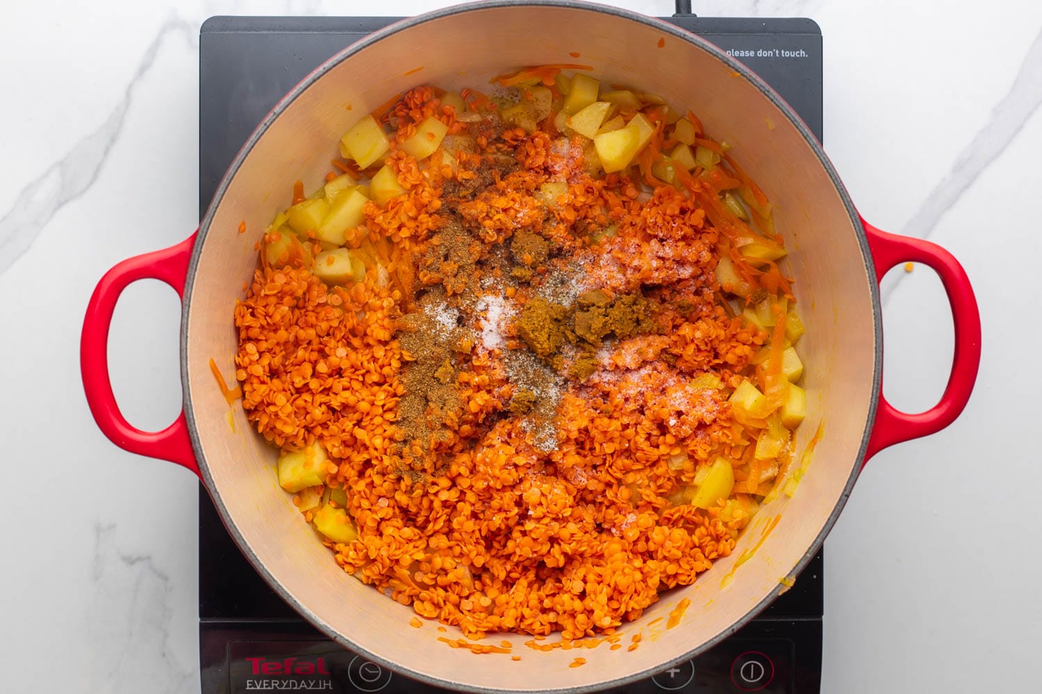 Red lentils and spices added to a dutch oven with potatoes and onions to make crushed lentil soup