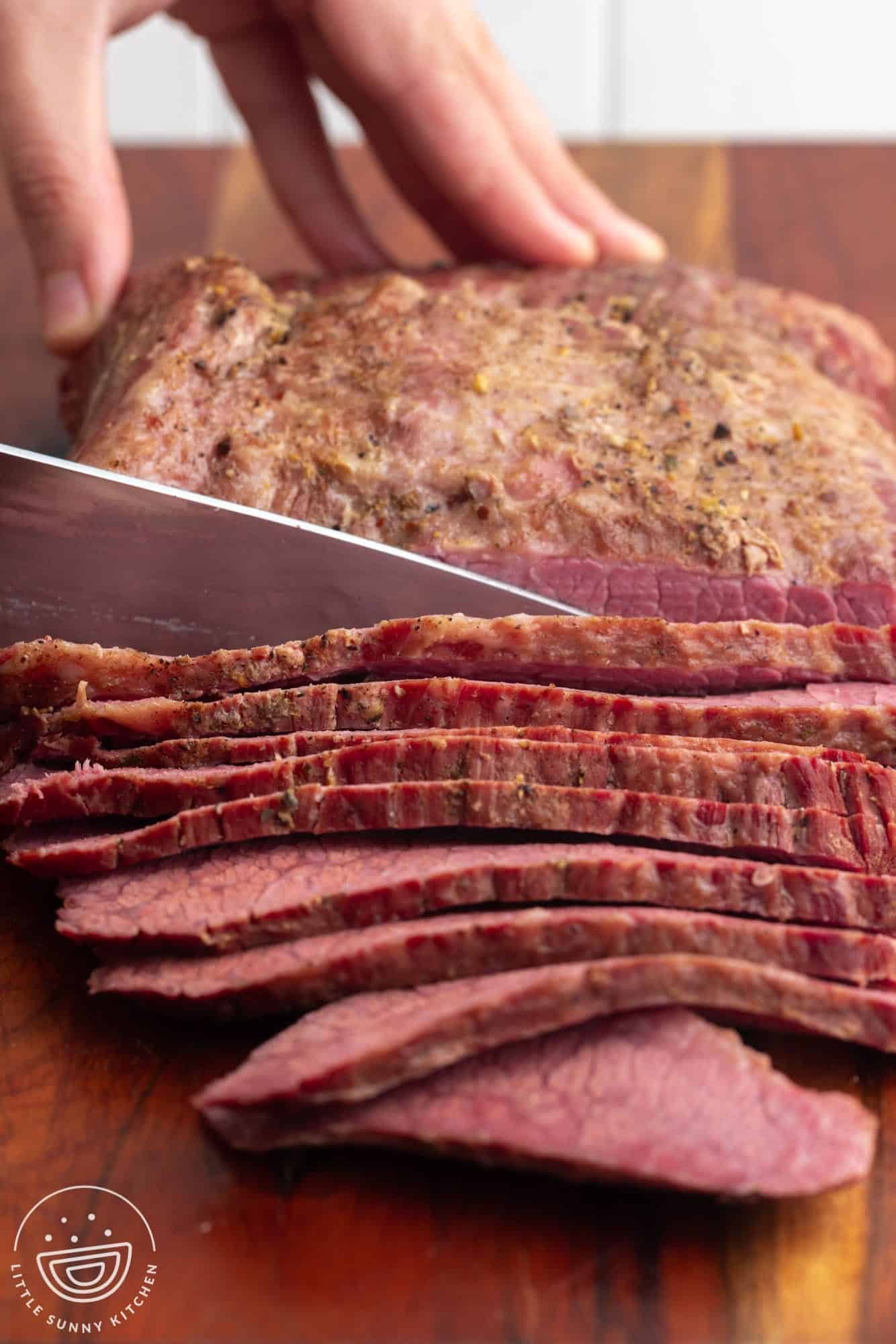 a corned beef brisket held with a hand and sliced thinly with a large knife.
