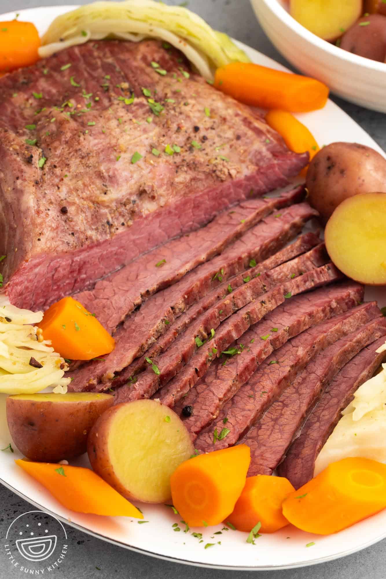 a platter of sliced corned beef with cabbage, carrots, and potatoes.
