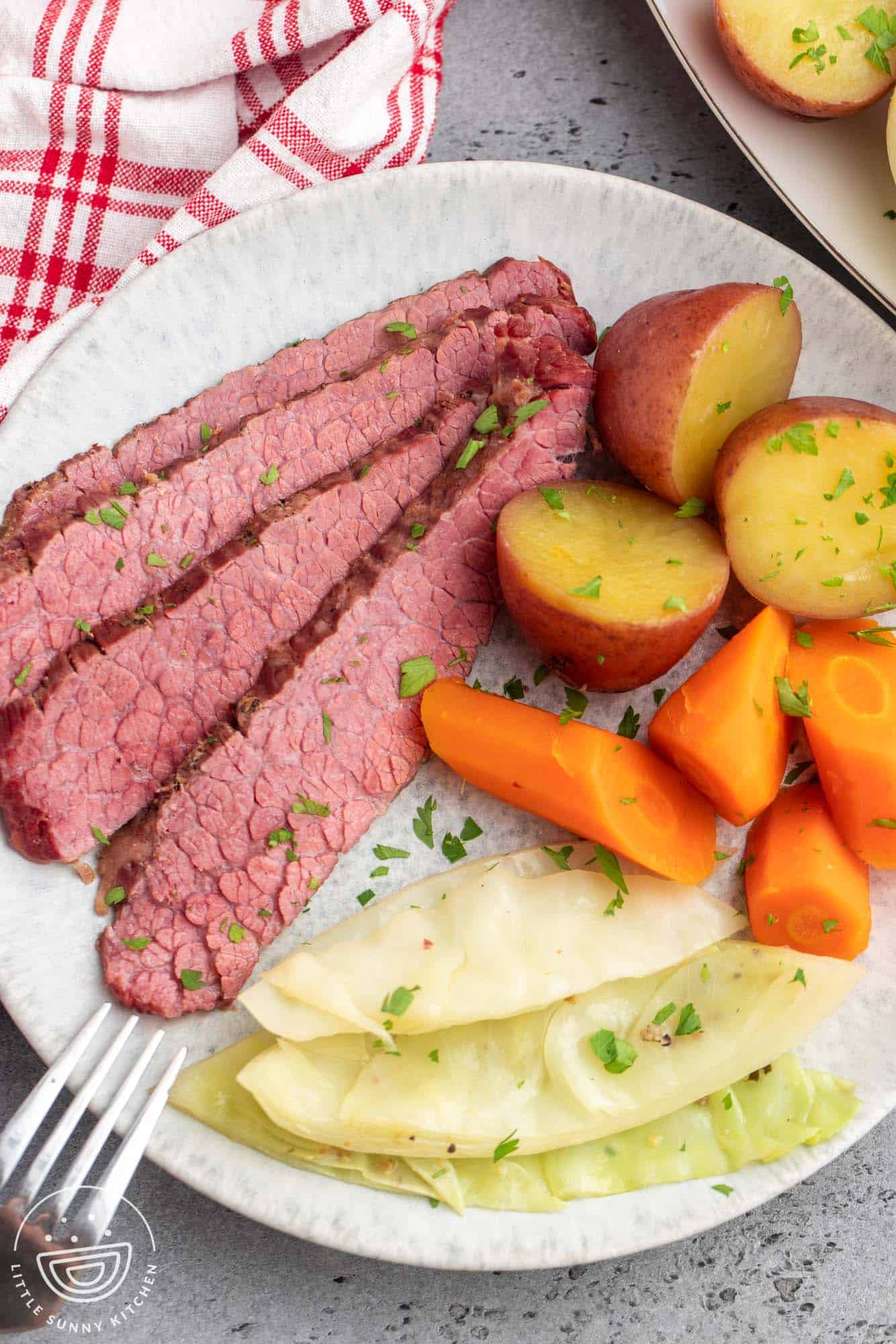 a dinner plate with four slices of corned beef, three pieces of red potato, four pieces of carrots, and a wedge of boiled cabbage.