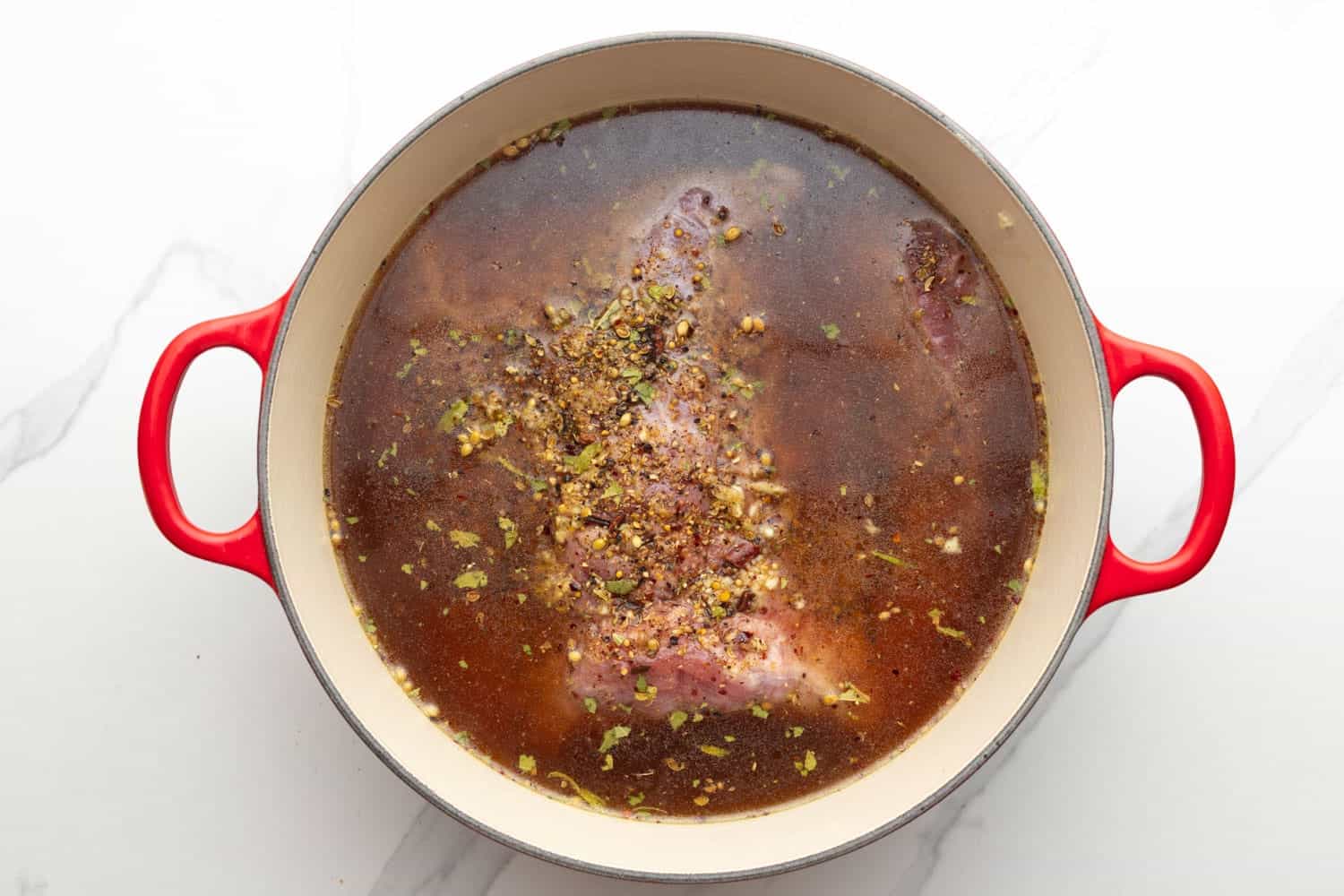 corned beef brisket in a dutch oven with garlic and herbs added to beef broth.