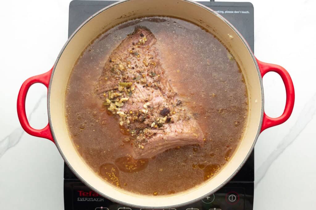 seasoned corned beef in a dutch oven with broth.