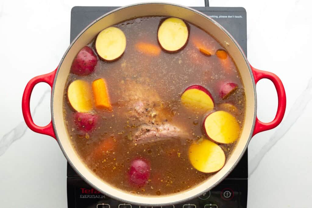 a dutch oven of broth, brisket, carrots and red potatoes.