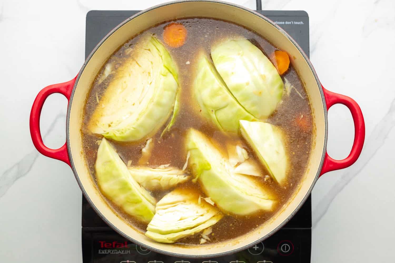 wedges of cabbage and carrots in a dutch oven with beef broth.