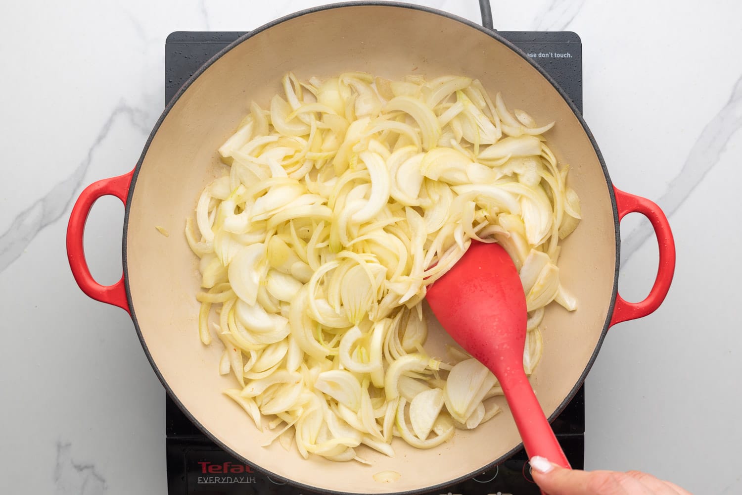 thinly sliced onions sauteed in a large skillet over an electric burner, stirred with a red spatula.