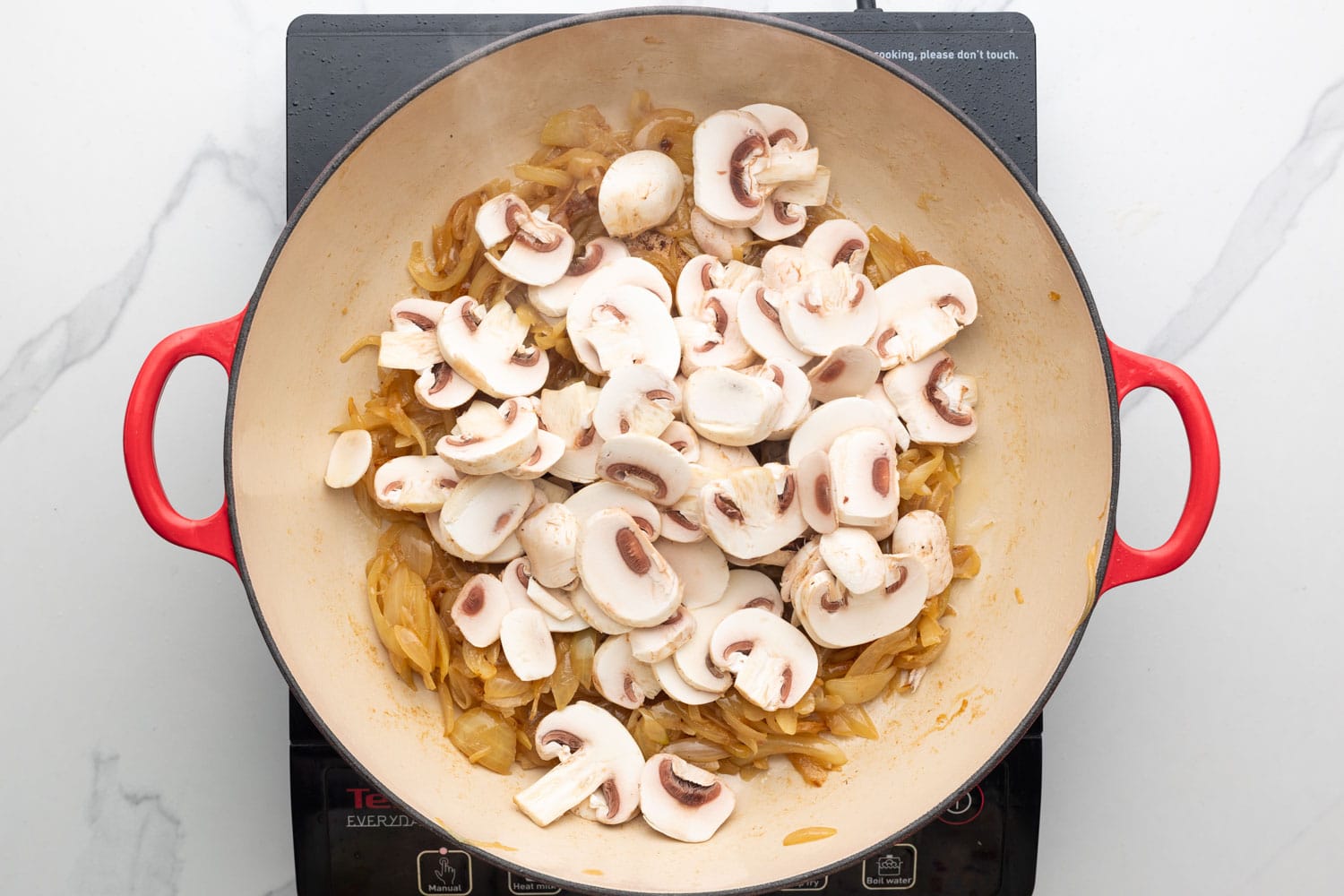 Fresh sliced mushrooms added to a skillet of caramelized onions.