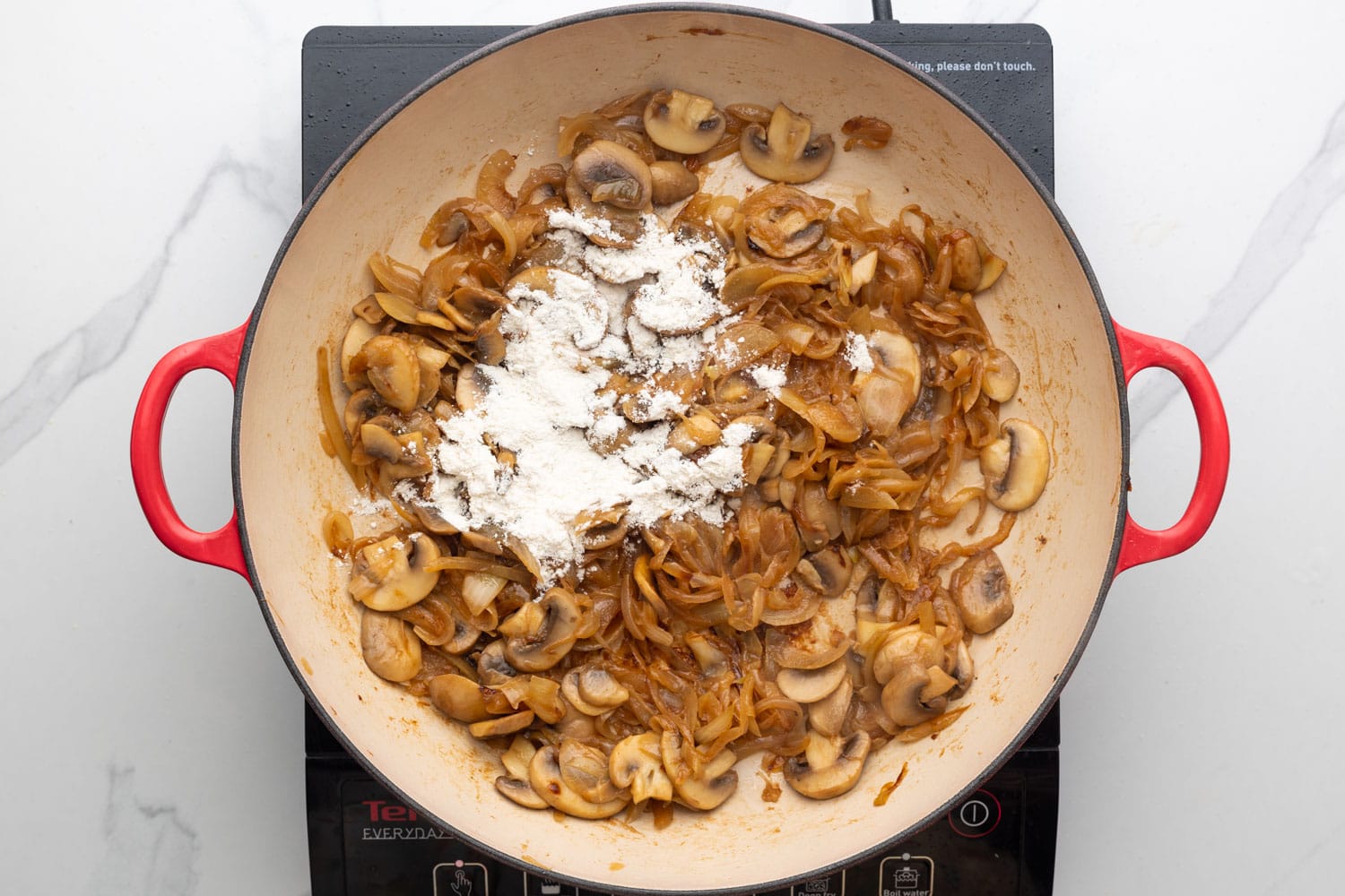 Flour added to caramelized onions and mushrooms in a pan.