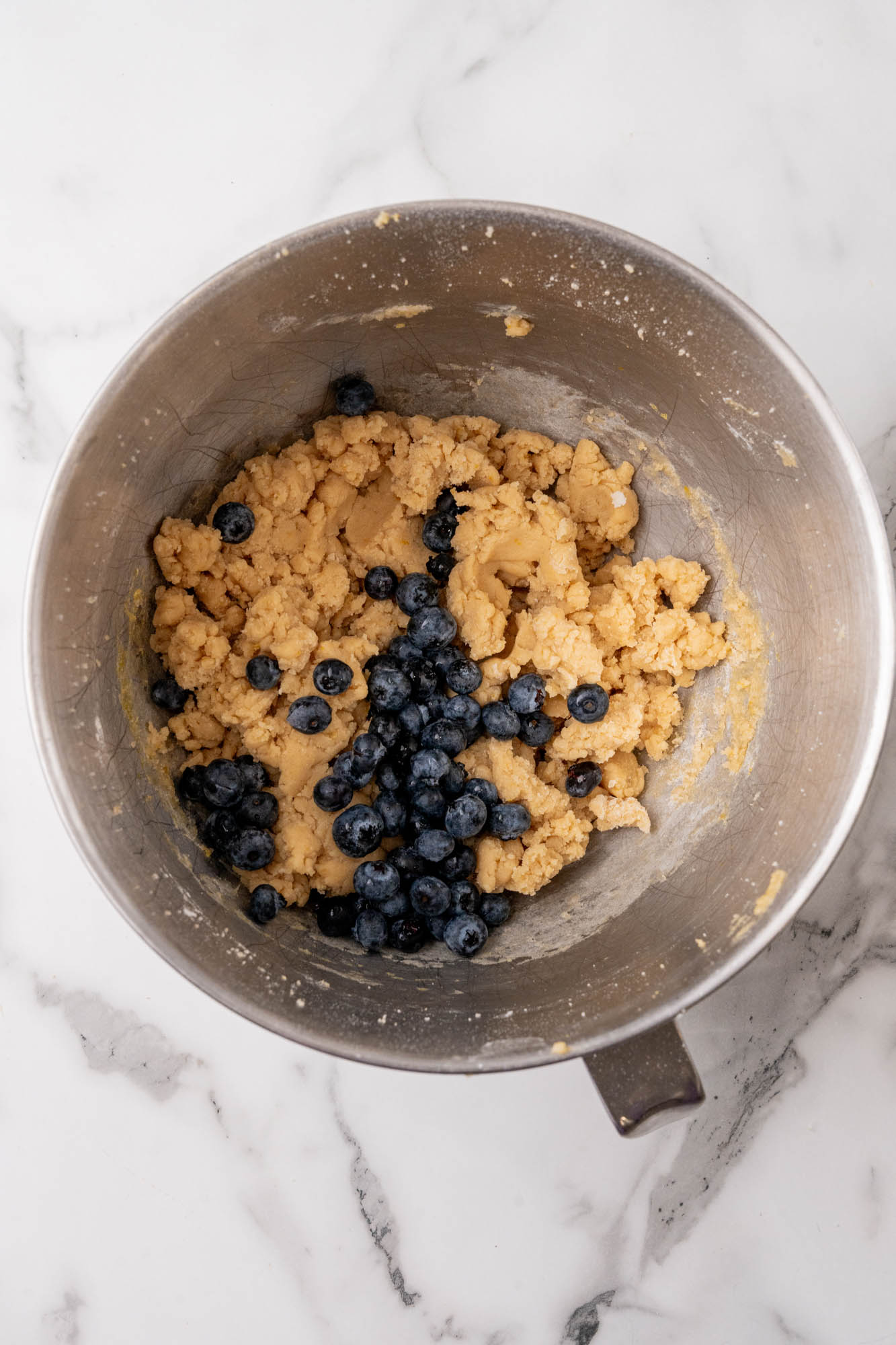 fresh blueberries added to cookie dough in a metal bowl.