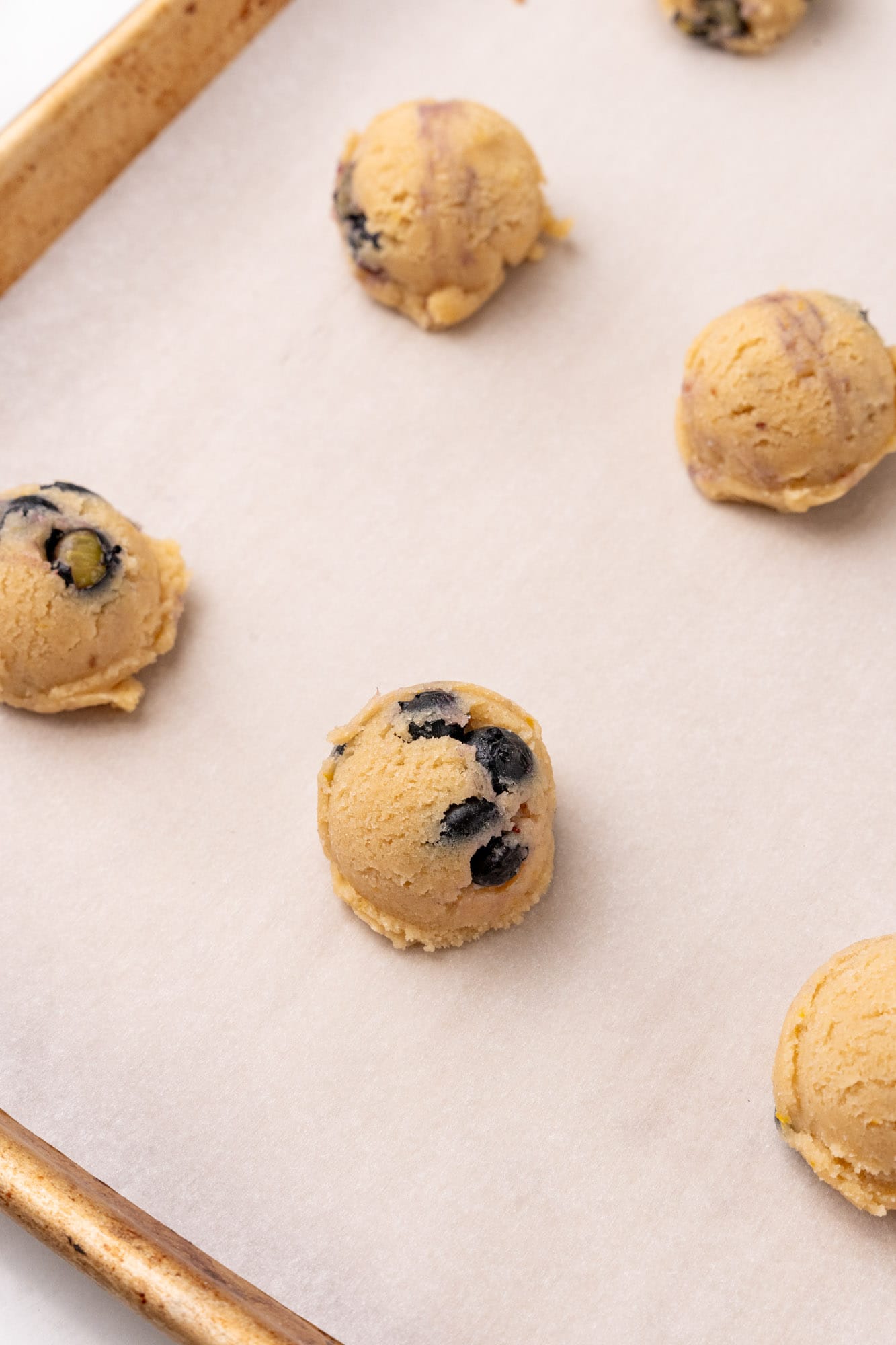 round balls of lemon blueberry cookie dough on a parchment lined baking sheet.