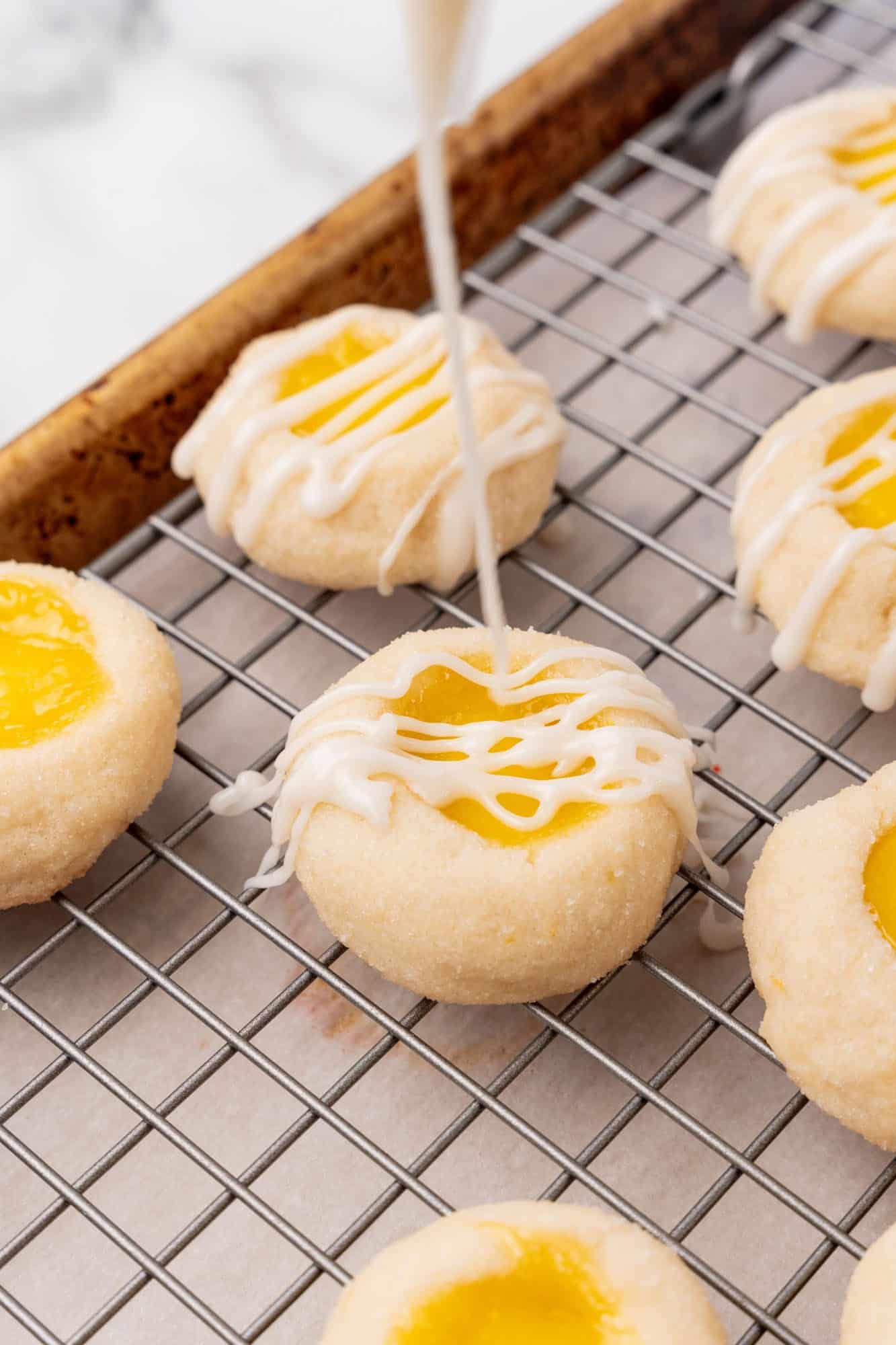 icing drizzling over lemon curd cookies on a wire rack.