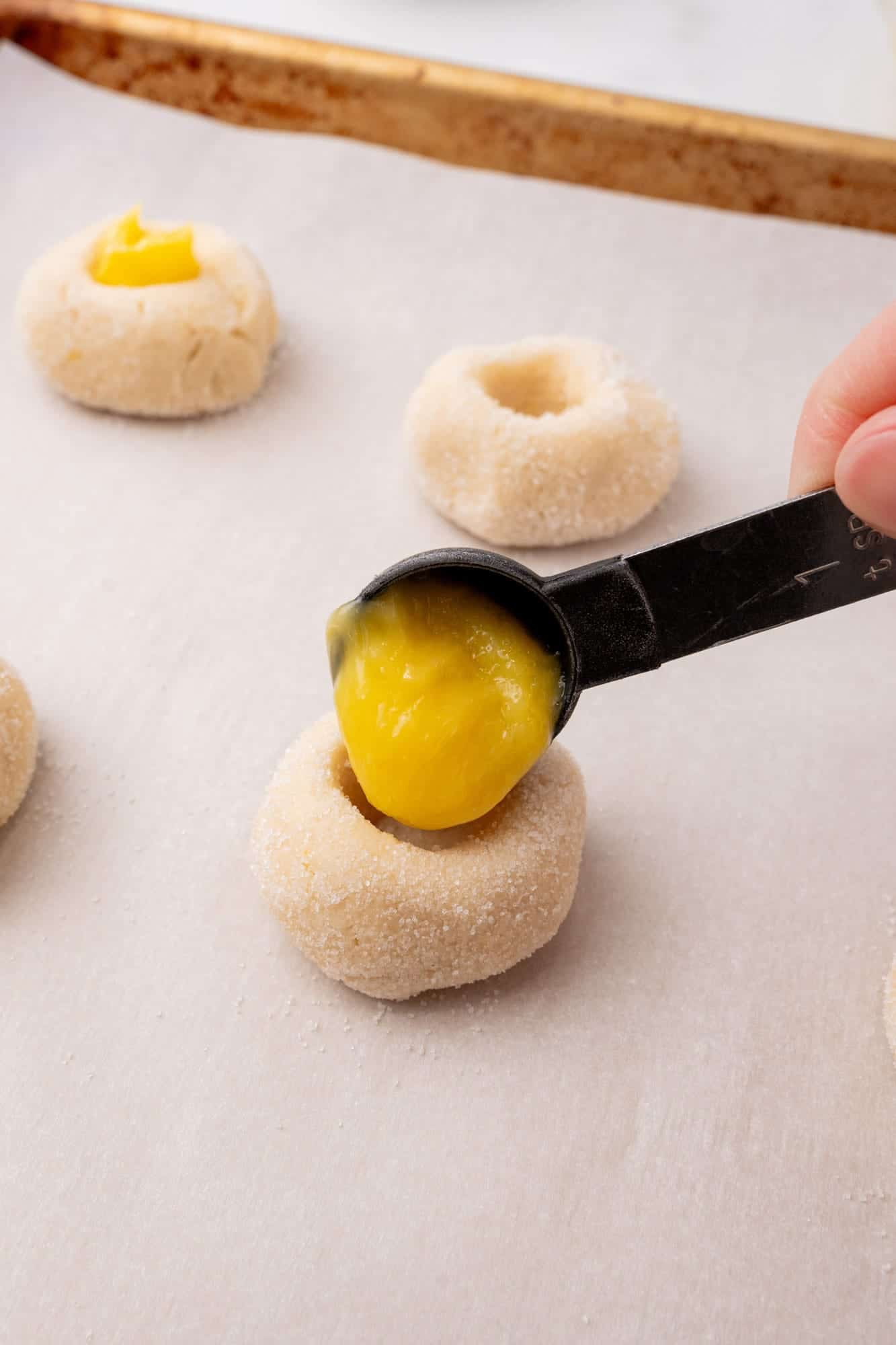 a teaspoon adding lemon curd to unbaked cookies with indentations.
