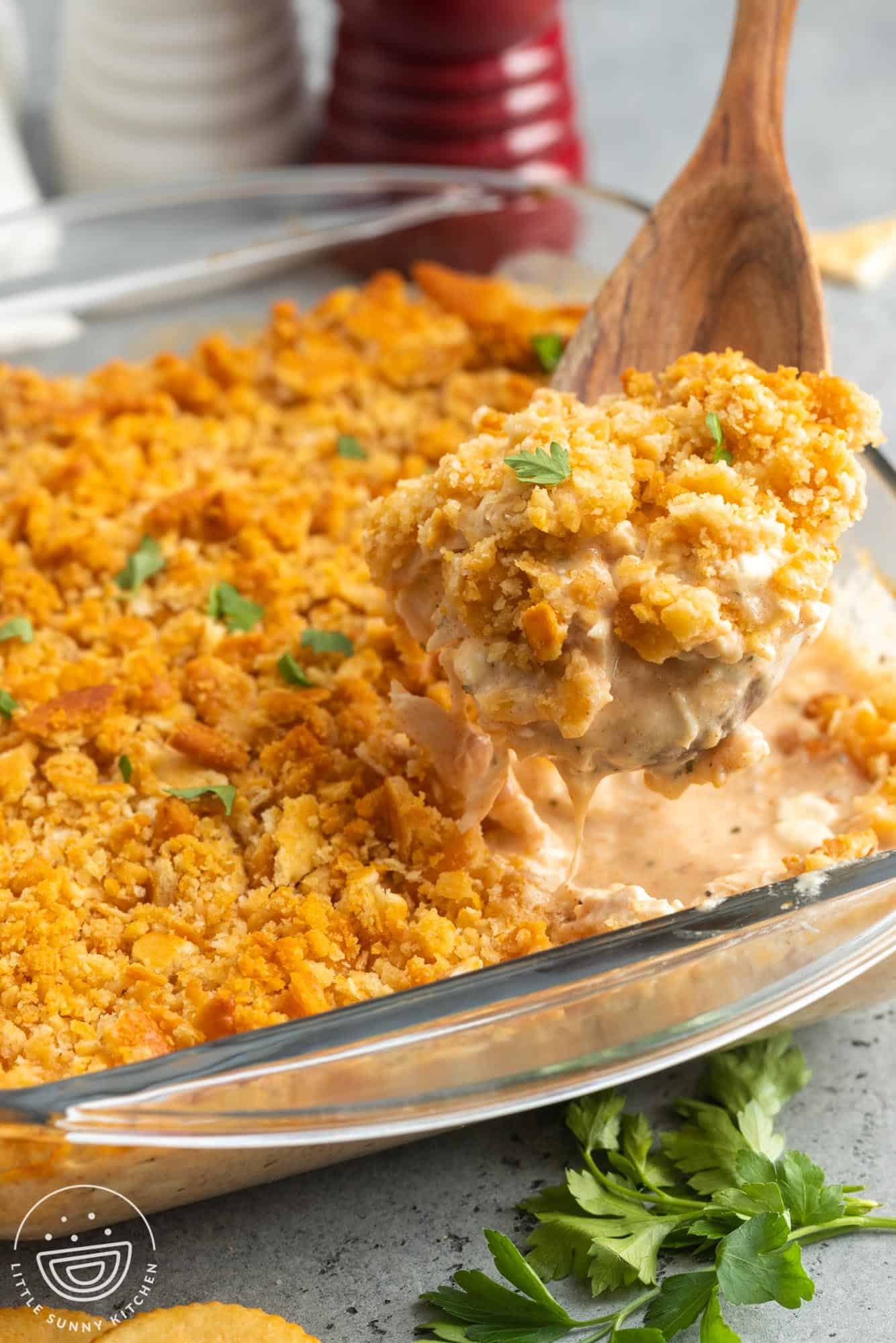 million dollar chicken casserole with crispy cracker topping, served with a wooden spoon.